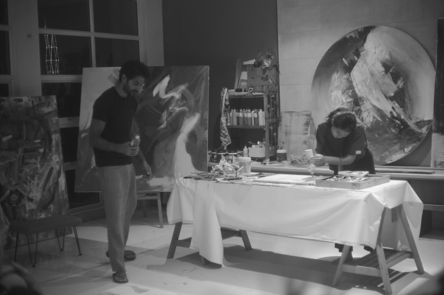 Wide view of the studio, canvases stacked and paint laid out on a trestle table