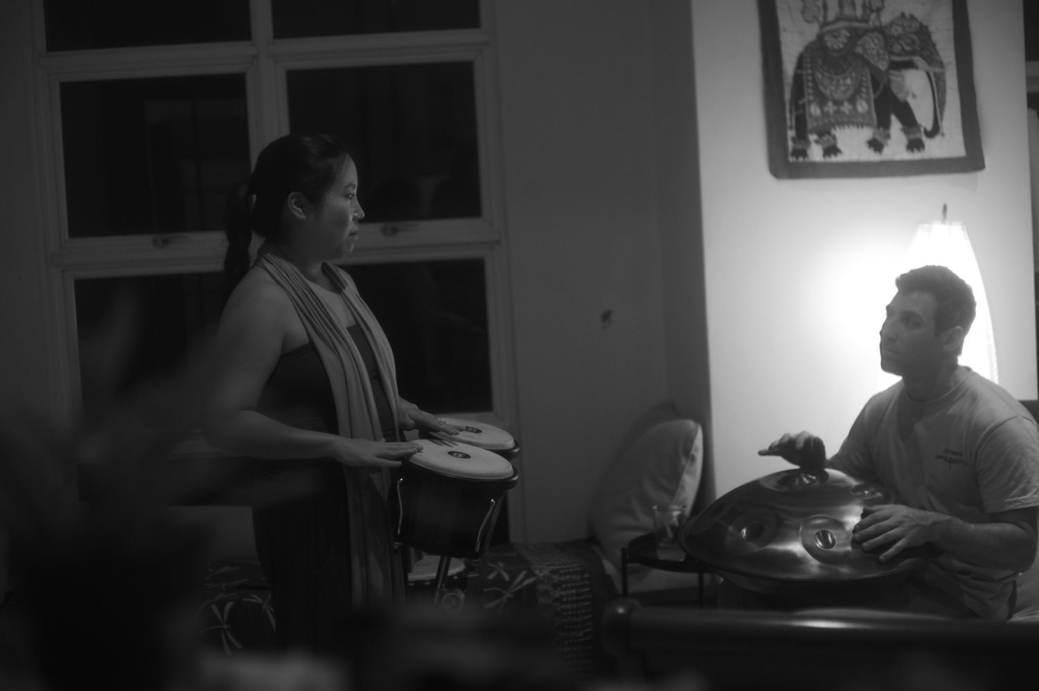A woman on bongos and a man on handpan, playing across the space from each other