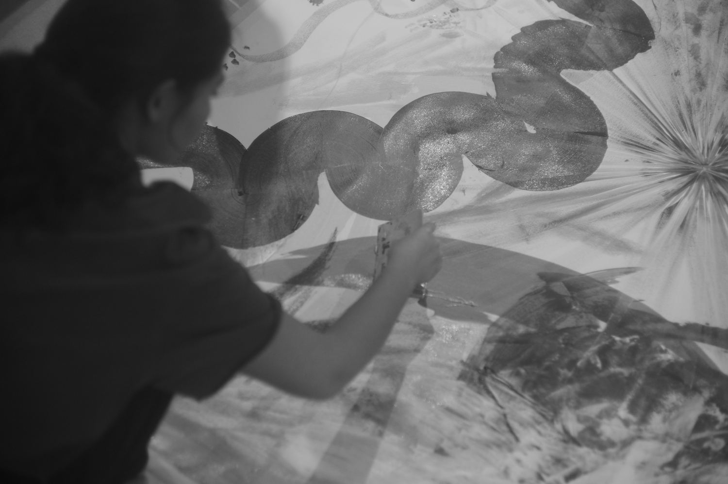 Close over-the-shoulder view of a squeegee pulling shapes through paint